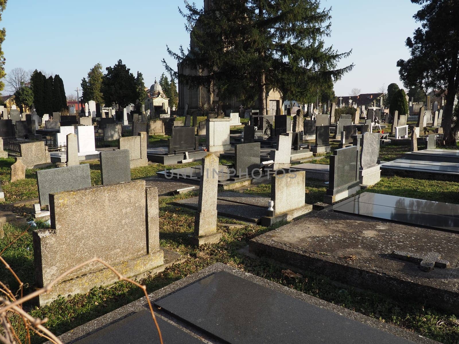 Sremska Mitrovica, Serbia, February 25, 2021. Christian city modern cemetery. Graves with stone monuments and crosses. Granite headstones. Crypt or chapel. Funeral or Halloween theme.