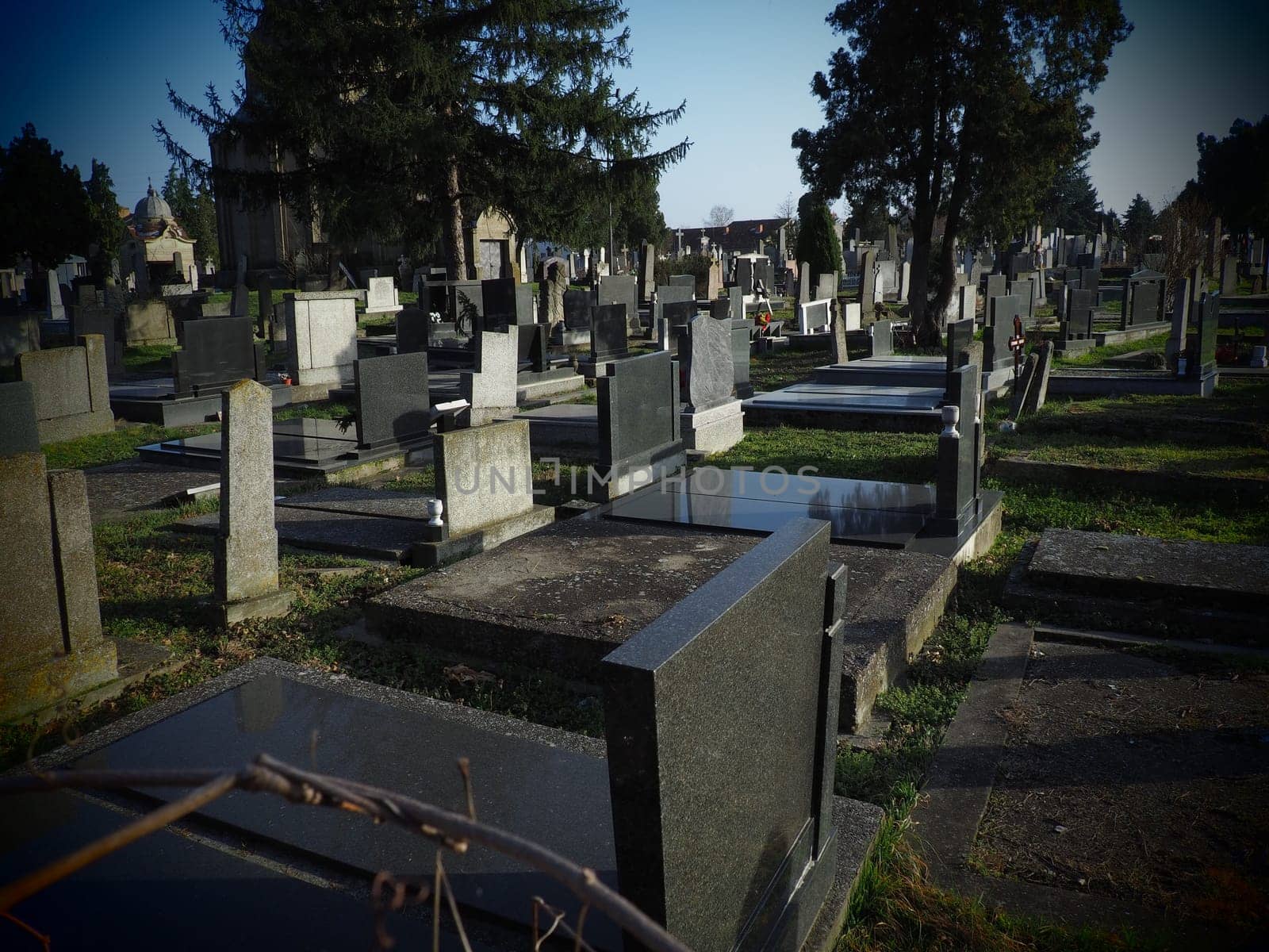 Sremska Mitrovica, Serbia, February 25, 2021. Christian city modern cemetery. Graves with stone monuments and crosses. Granite headstones. Crypt or chapel. Funeral or Halloween theme.