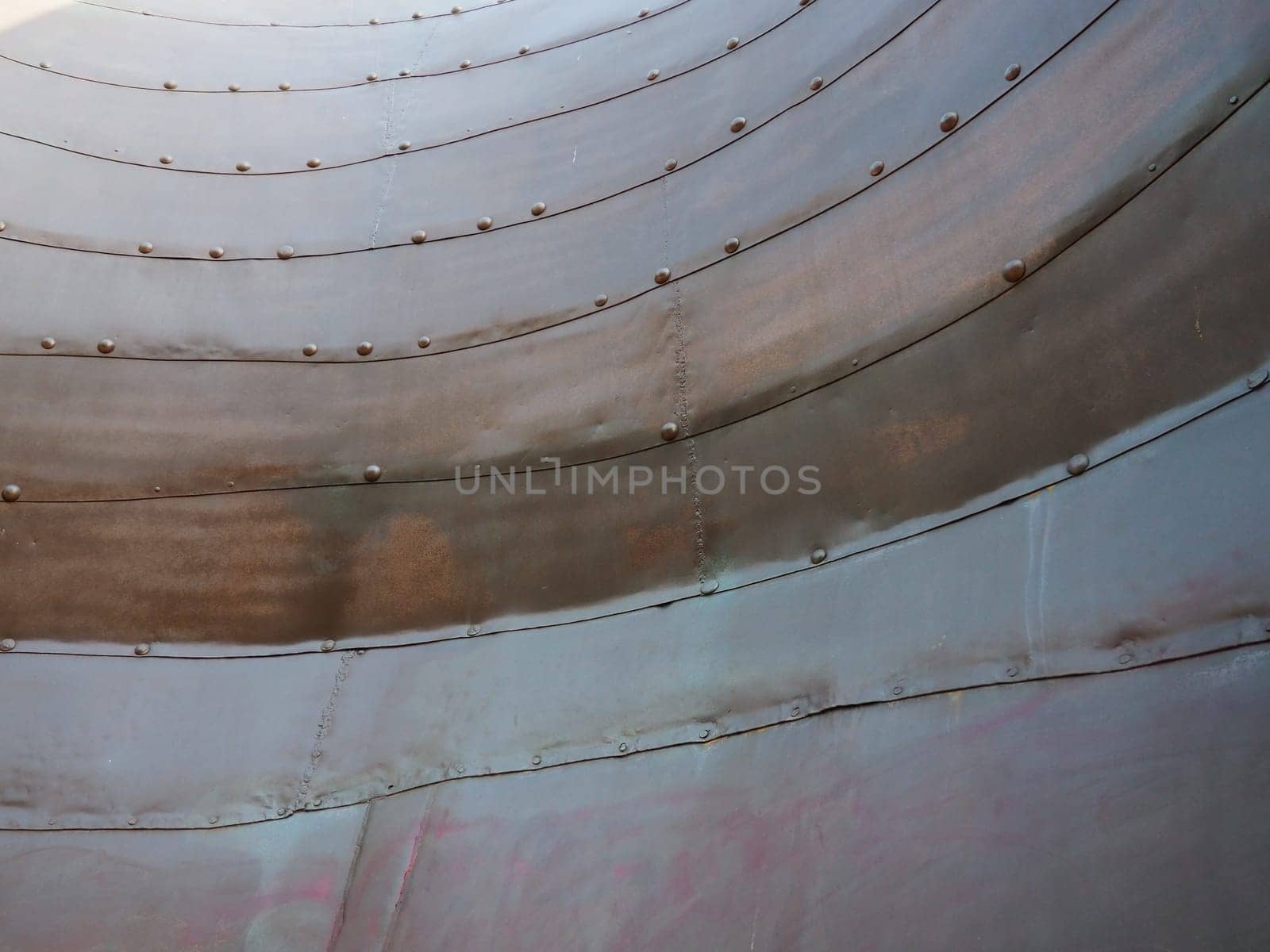 Metal surface with rivets and bolts. Abstract background of a military or industrial nature. Sheathing with dents, seams and nuts. Fasteners on metal. Steel or bronze panel.