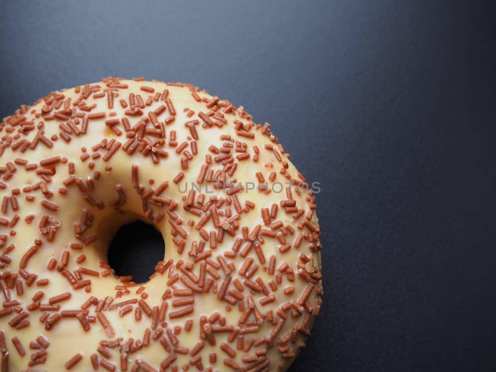 A doughnut or donut. A type of leavened fried dough. Sweet snack that can be homemade or purchased in bakeries, supermarkets, food stalls. Delicious pie with light icing on black or gray background.