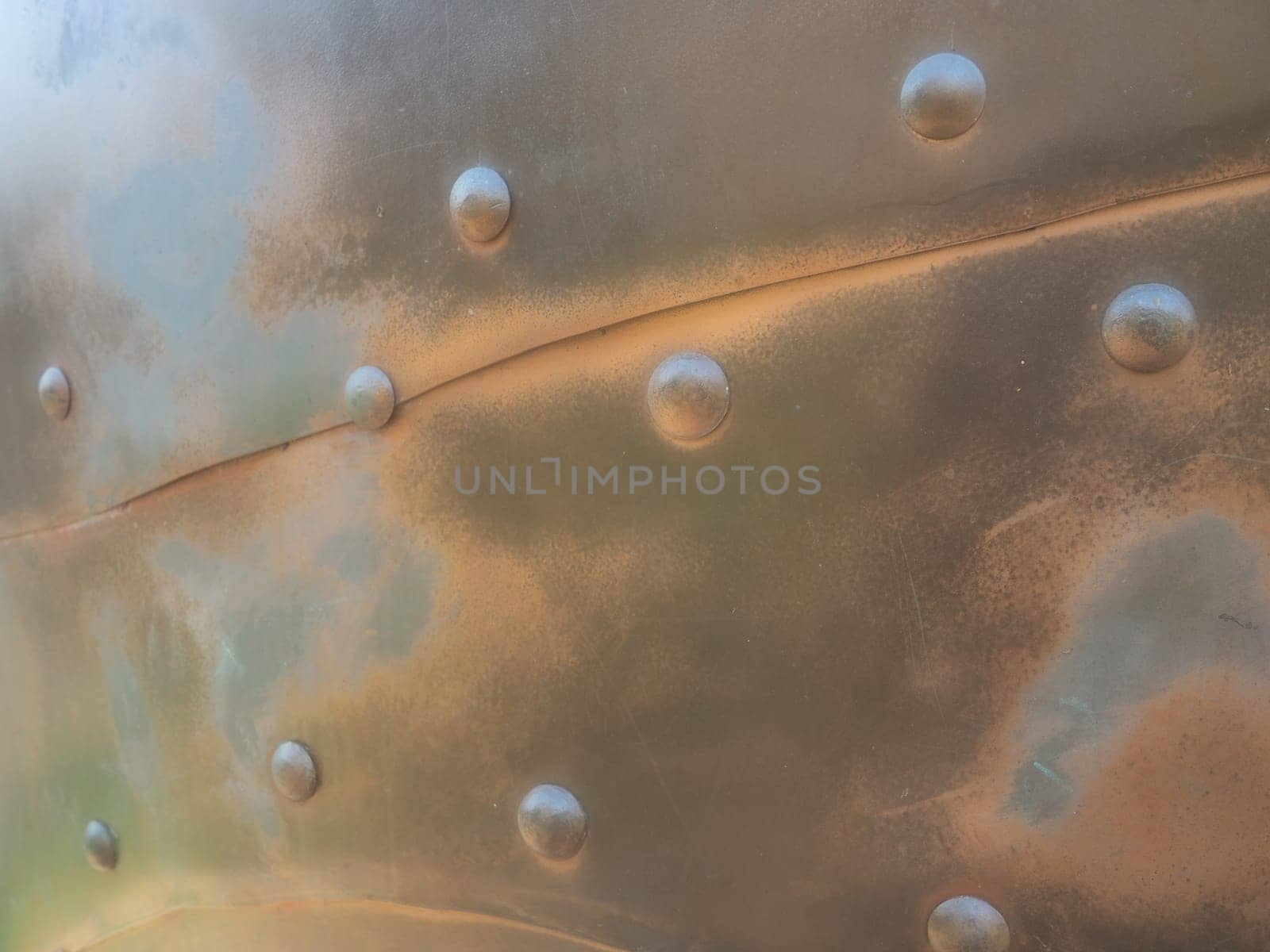 Metal surface with rivets and bolts. Abstract background of a military or industrial nature. Sheathing with dents, seams and nuts. Fasteners on metal. Steel or bronze panel.