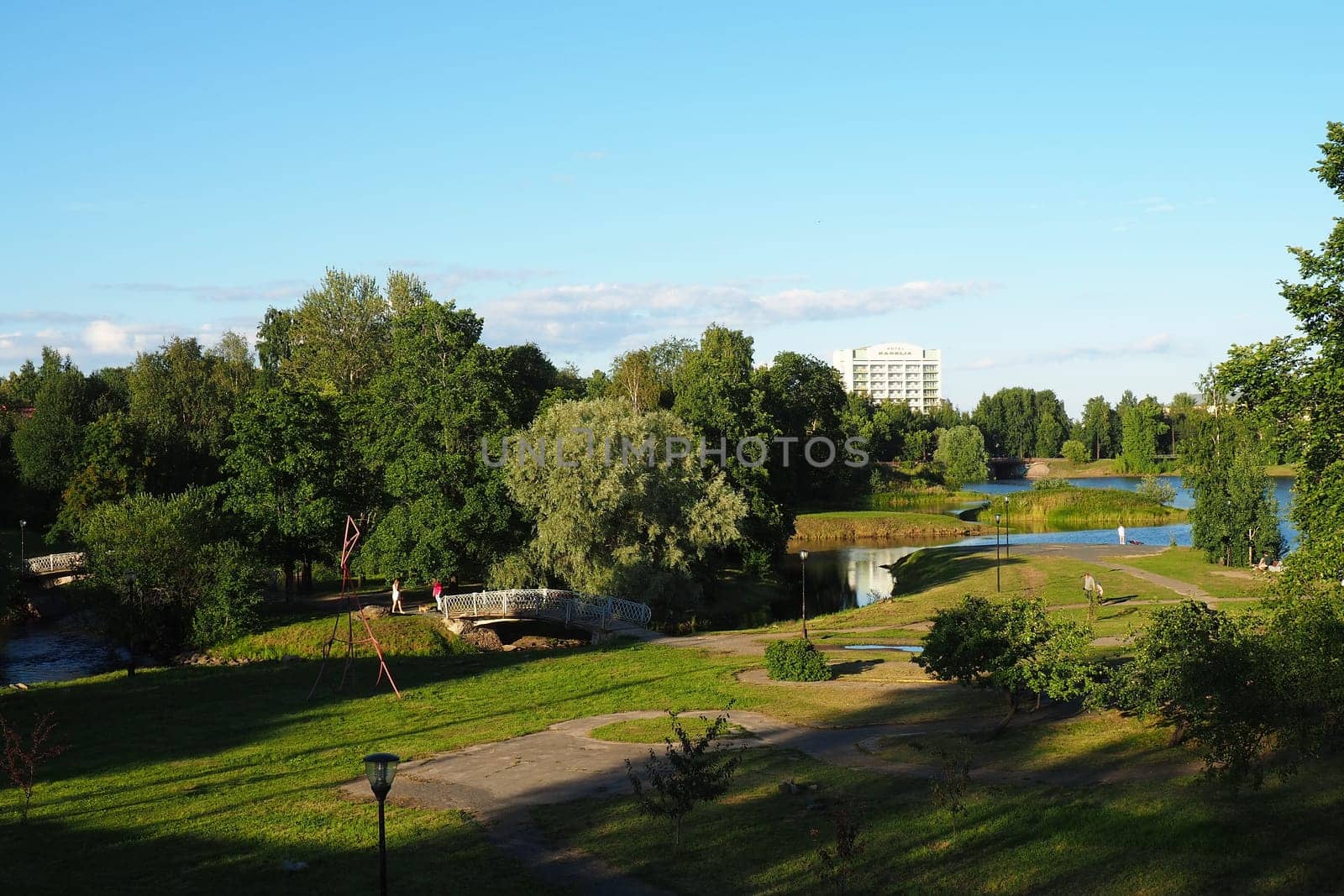 Mouth, floodplain and terraces of the Lososinka River, Petrozavodsk, Republic of Karelia August 3, 2022. Sunny windless evening. Bushes and trees. Passers-by people cross the river through the bridge