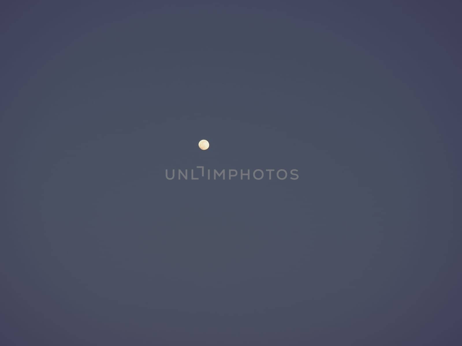 Moon in the night blue sky. White point in the sky. Dark vignetting around the edges of the image