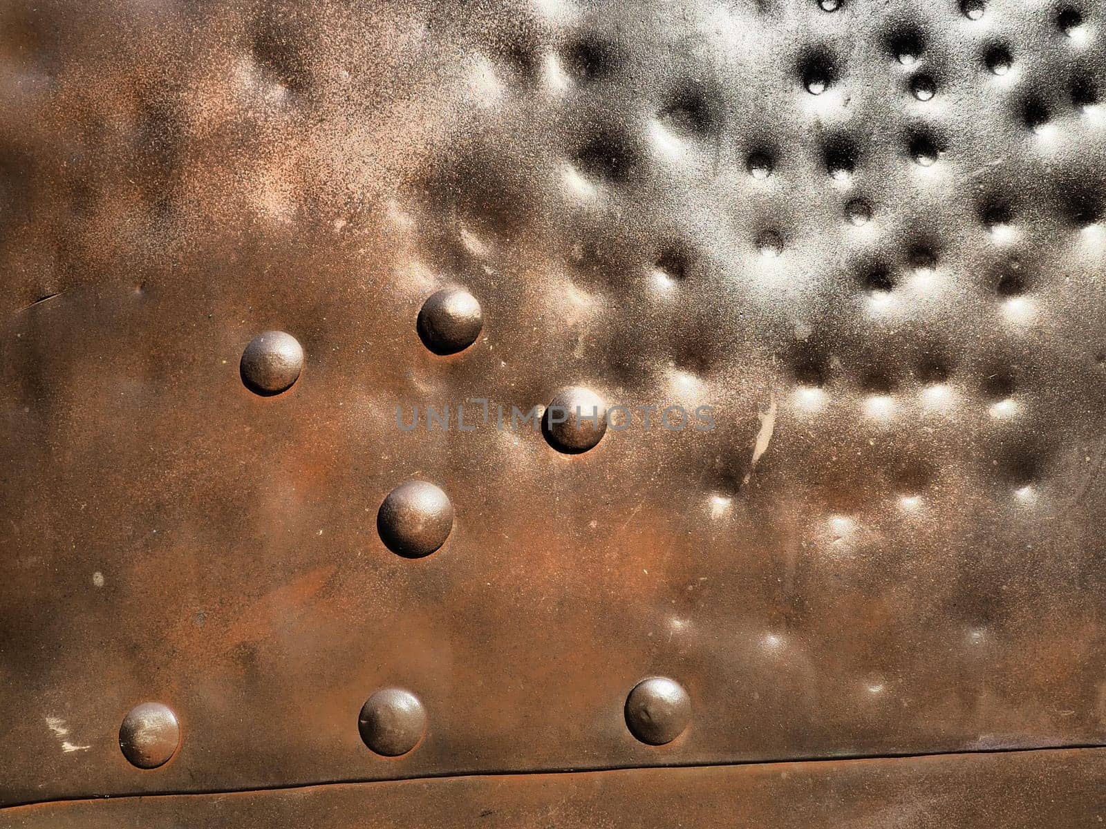 Metal surface with rivets and bolts. Abstract background of a military or industrial nature. Sheathing with dents, seams and nuts. Fasteners on metal. Steel or bronze panel.