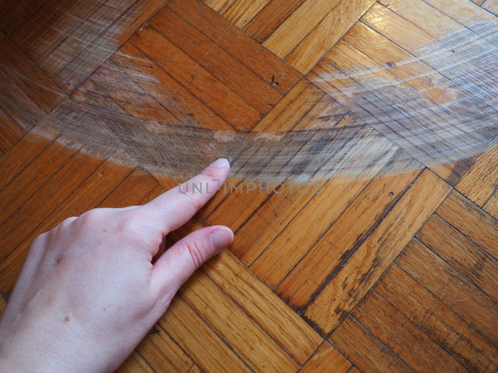 Scratched parquet flooring in the room. Scratches, chips and dents on the floor. Parquet in need of repair. The hand shows the size and length of the scratch on the parquet.