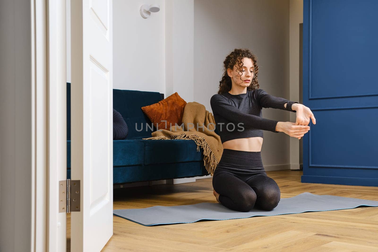 Young woman stretching arm muscles sitting on yoga mat at home