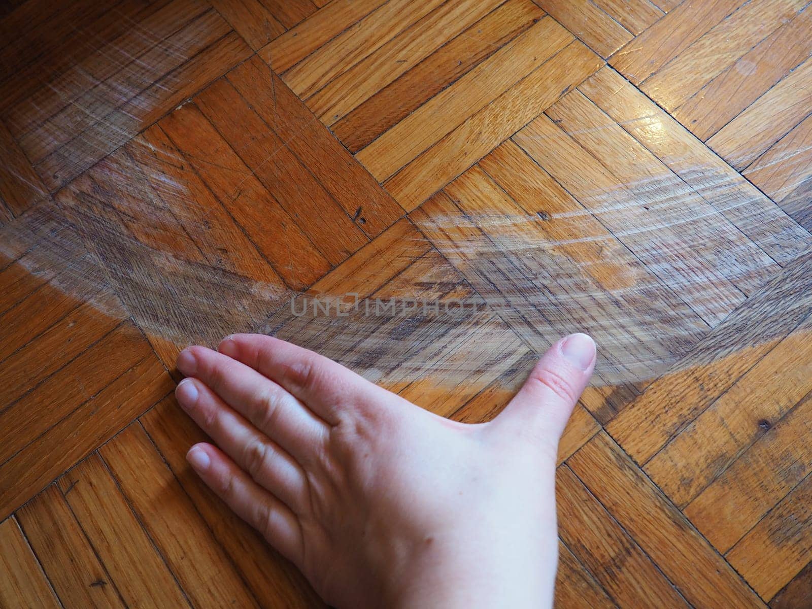 Scratched parquet flooring in the room. Scratches, chips and dents on the floor. Parquet in need of repair. The hand shows the size and length of the scratch on the parquet.