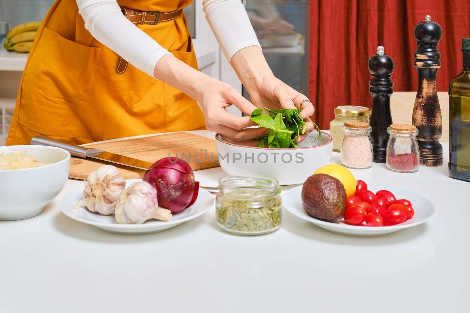 Female hands tossing fresh spinach leaves for probiotic salad in the bowl closeup