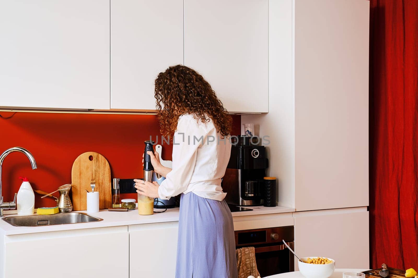 Woman using electric blender to make hummus at home, back view