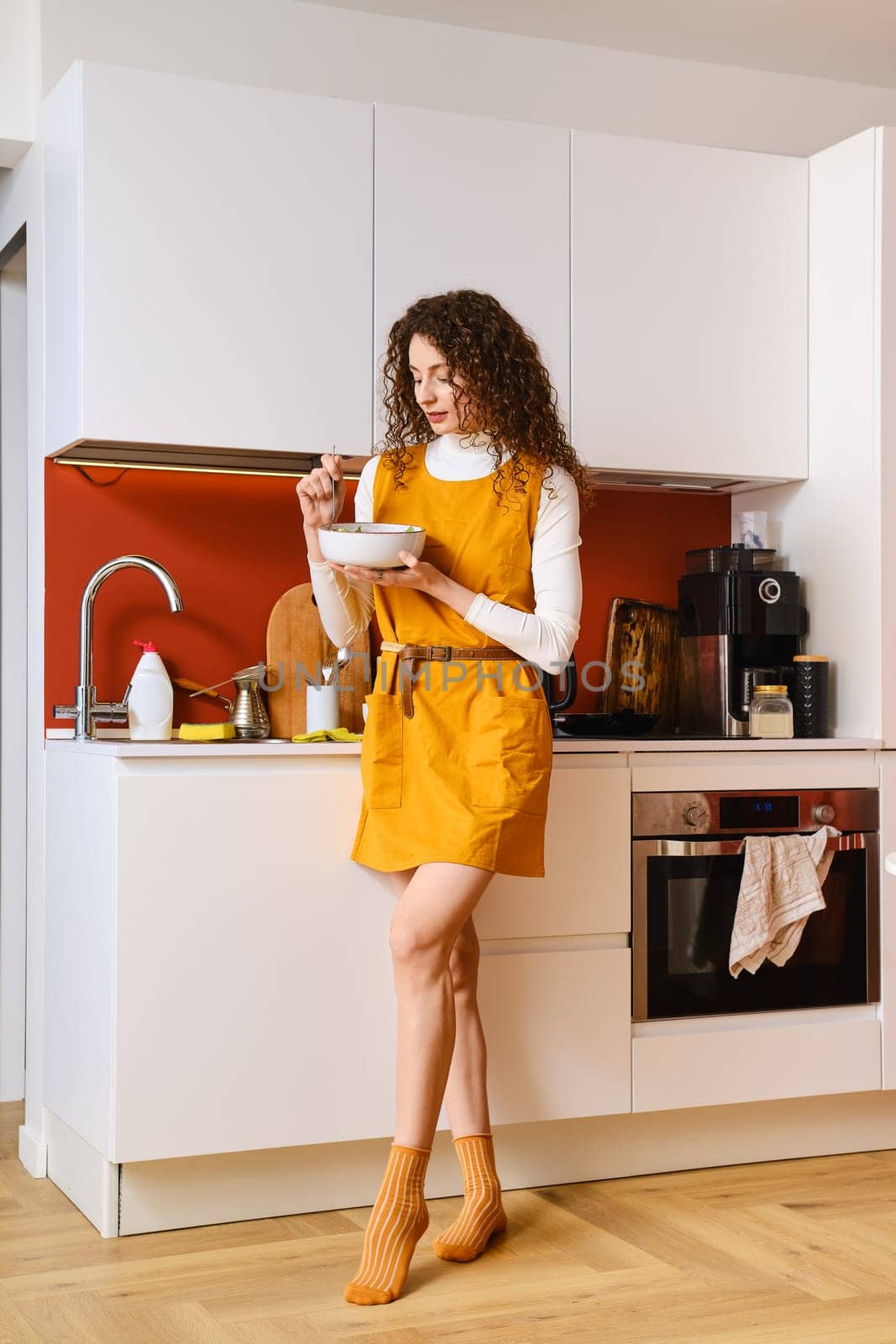 Slim woman eating salad in a hurry standing in the kitchen