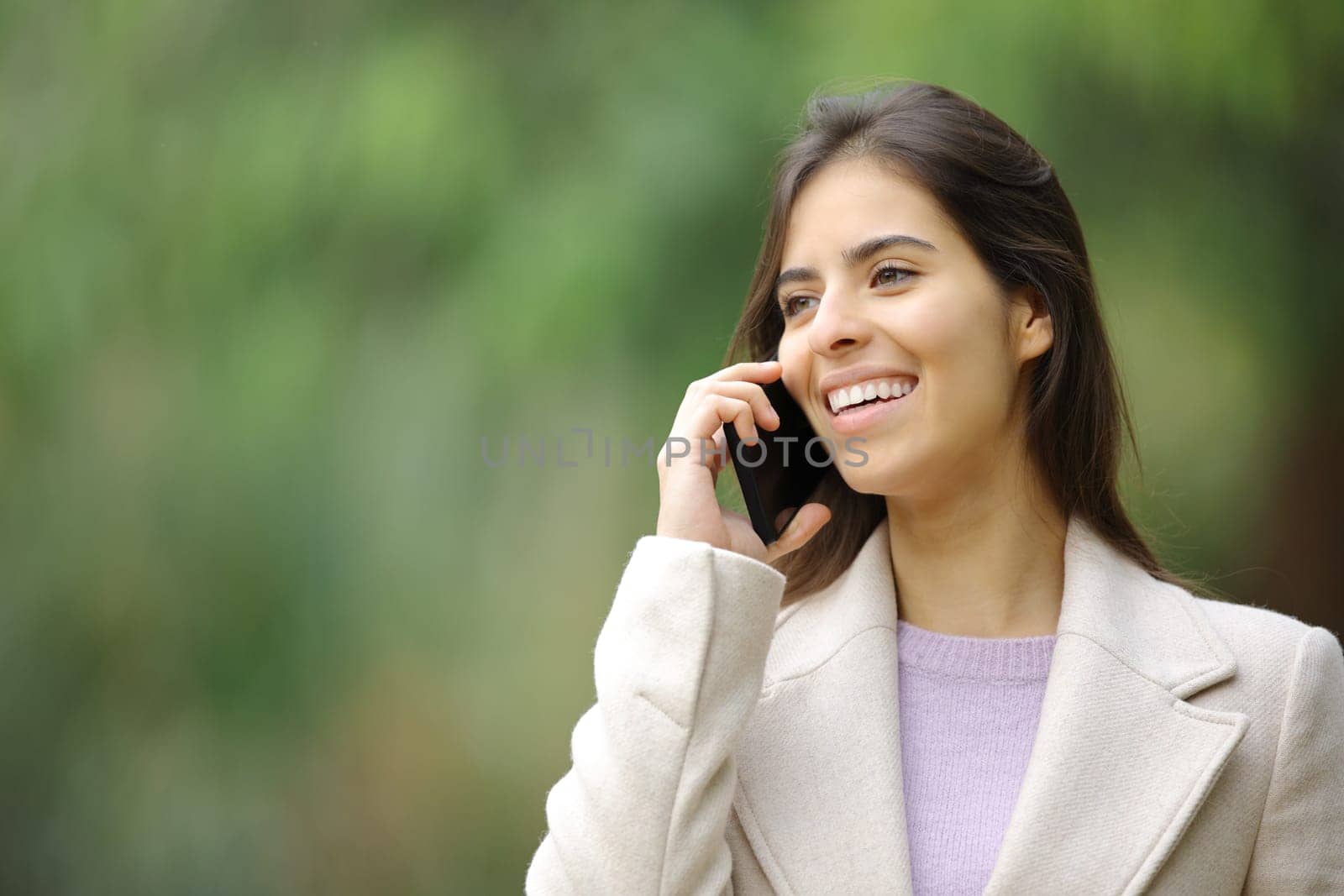 Happy woman in winter talks on smart phone walking in a park