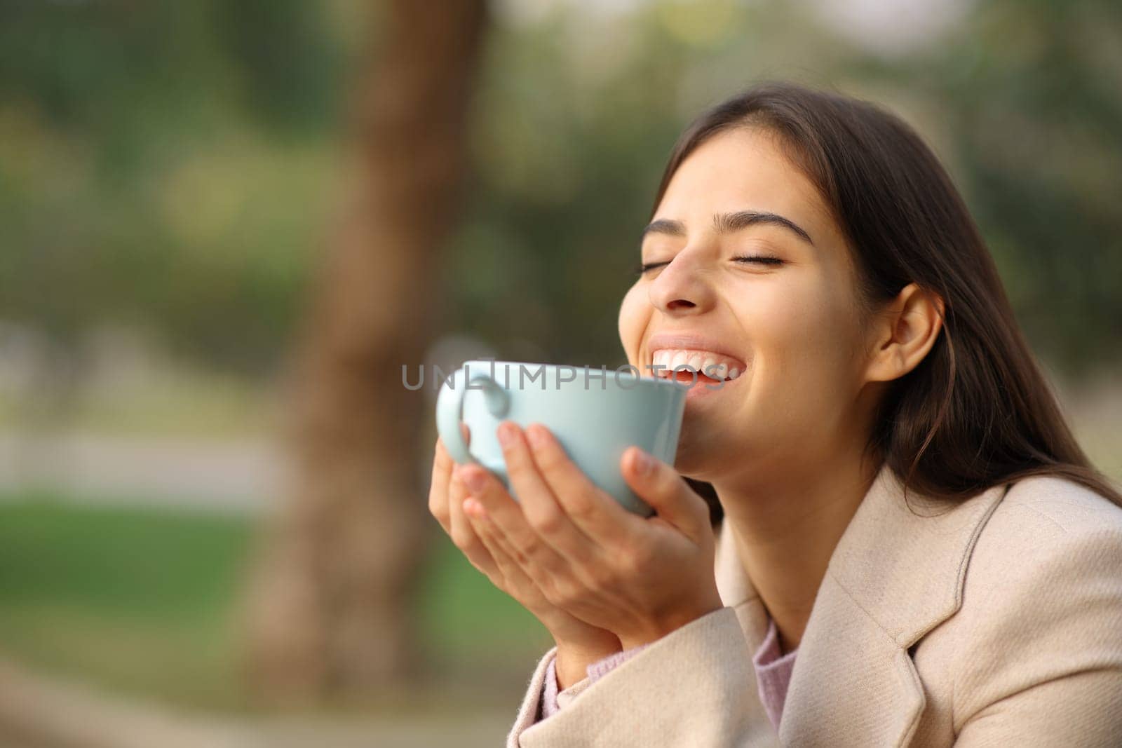 Happy woman in winter enjoying coffee laughing in a park