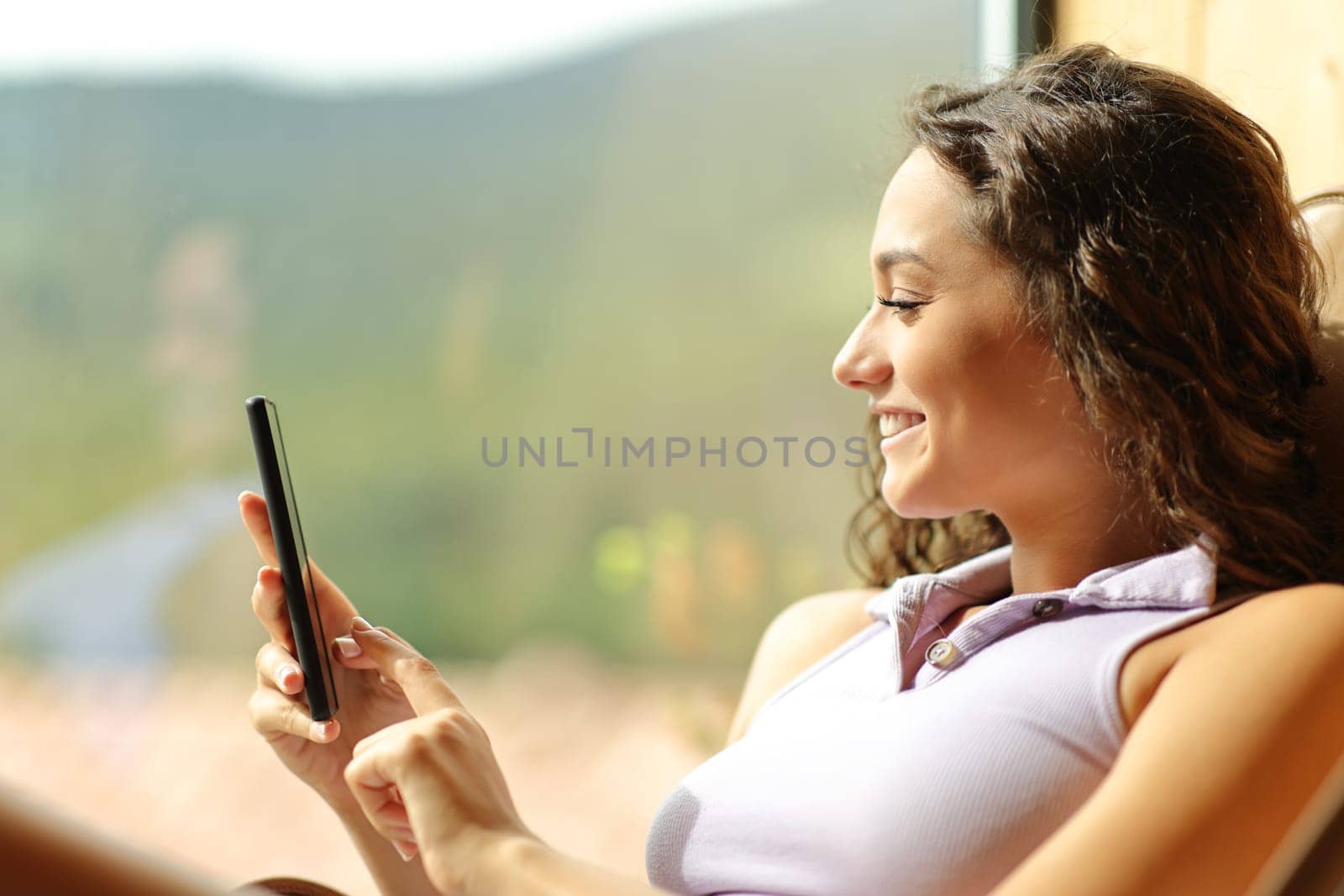 Happy woman using cell phone on a chair at home