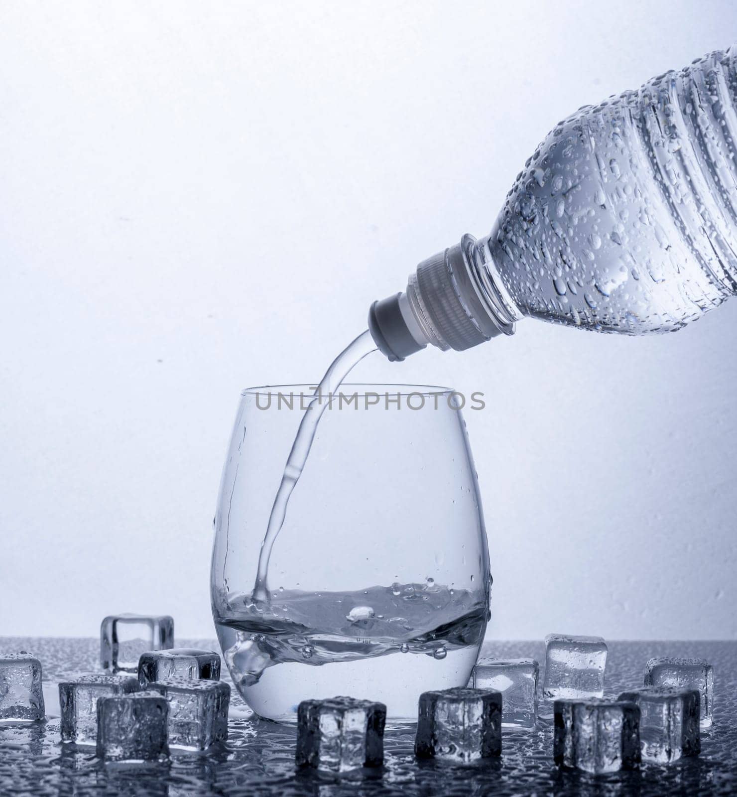 Pouring fresh drinking mineral water from plastic bottle. Glass filled with water over white background.