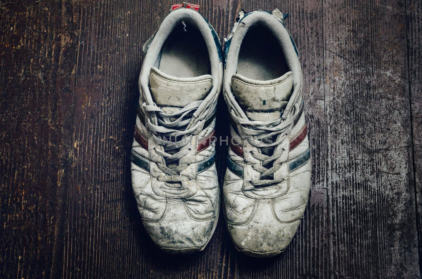 Dirty old sport shoes on rustic wooden background. Vintage worn sneakers still life from above..