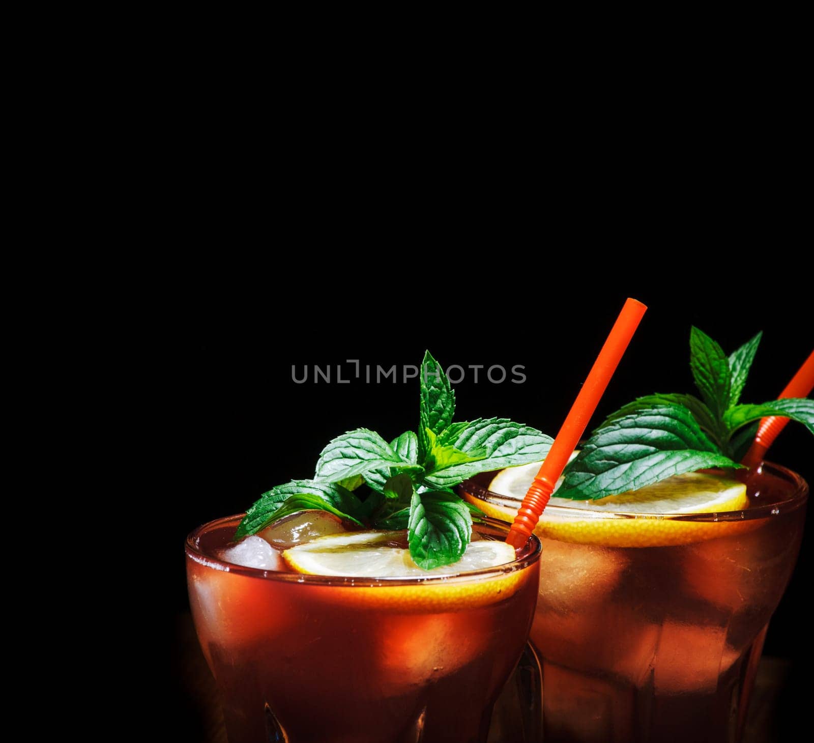 Cuba libre cocktail with ice, mint and lemon over black background. Alcohol beverage with rum and cola drink. Cocktail design menu background.