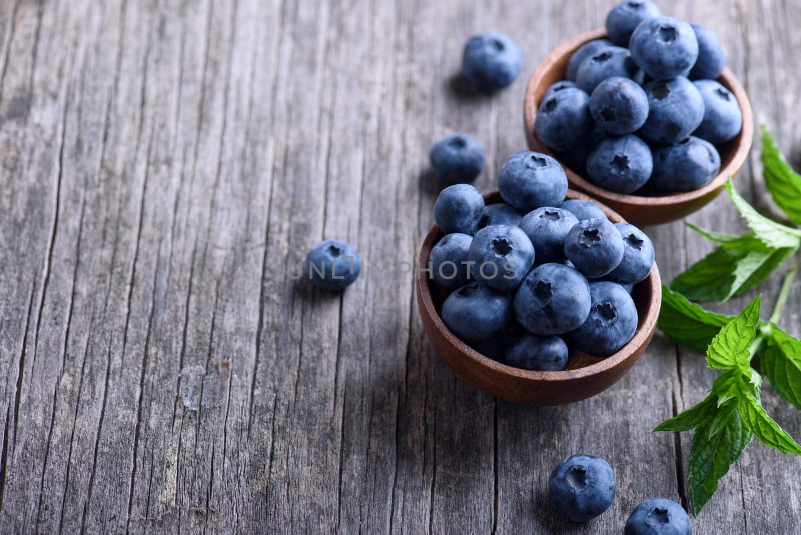 Bowl of fresh blueberries on rustic wooden table. Healthy organic seasonal fruit background. Organic food blueberries and mint leaf for healthy lifestyle.