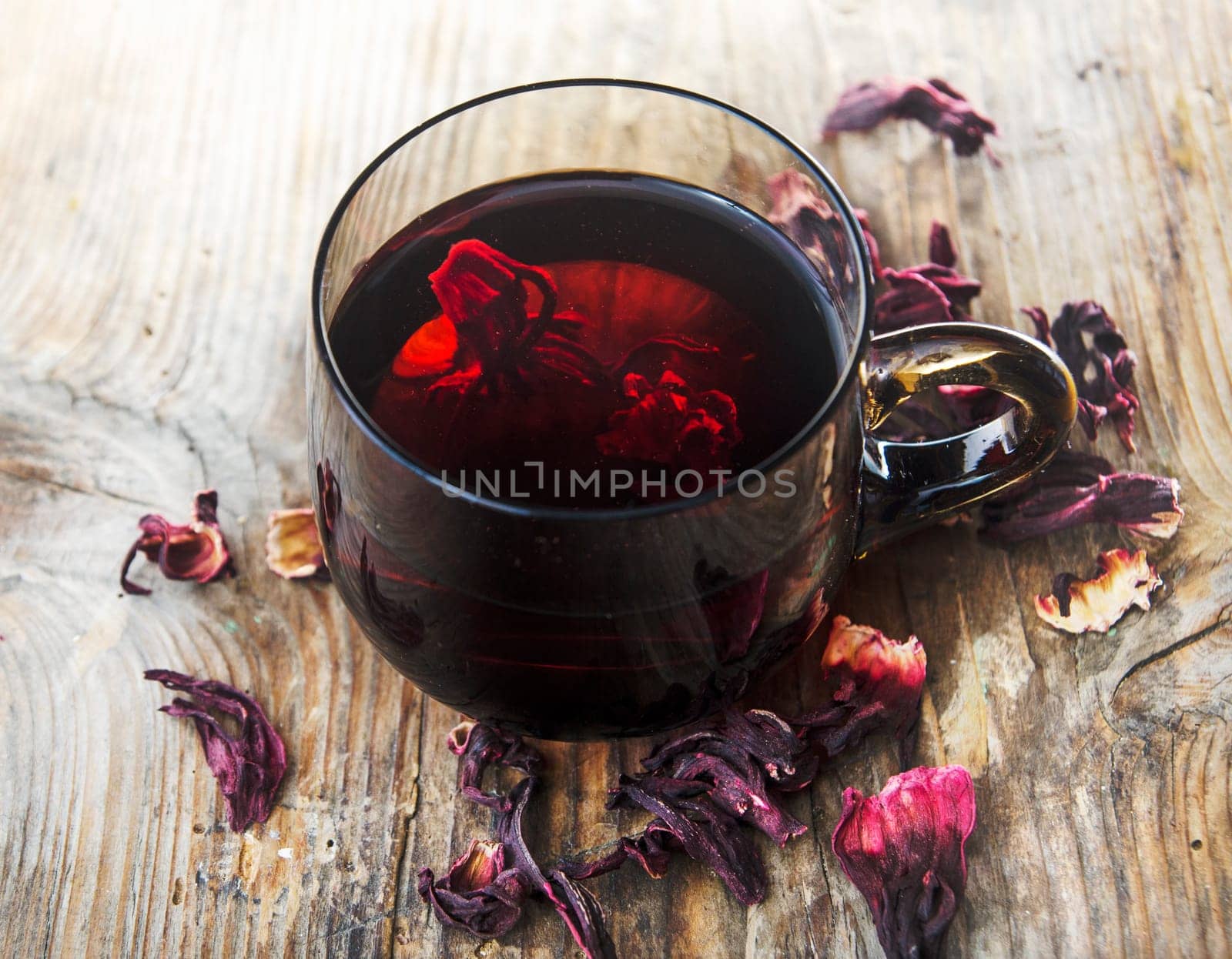 Hibiscus tea in teacup with dry hibiscus flower leaves. Organic herbal cup of tea on vintage wooden table background.