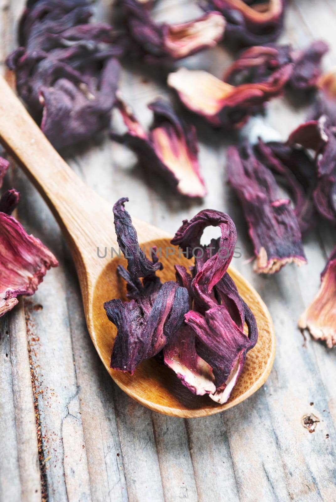Dry hibiscus flower leaves in wooden spoon from above. Organic asian red herbal tea on vintage wooden table background.