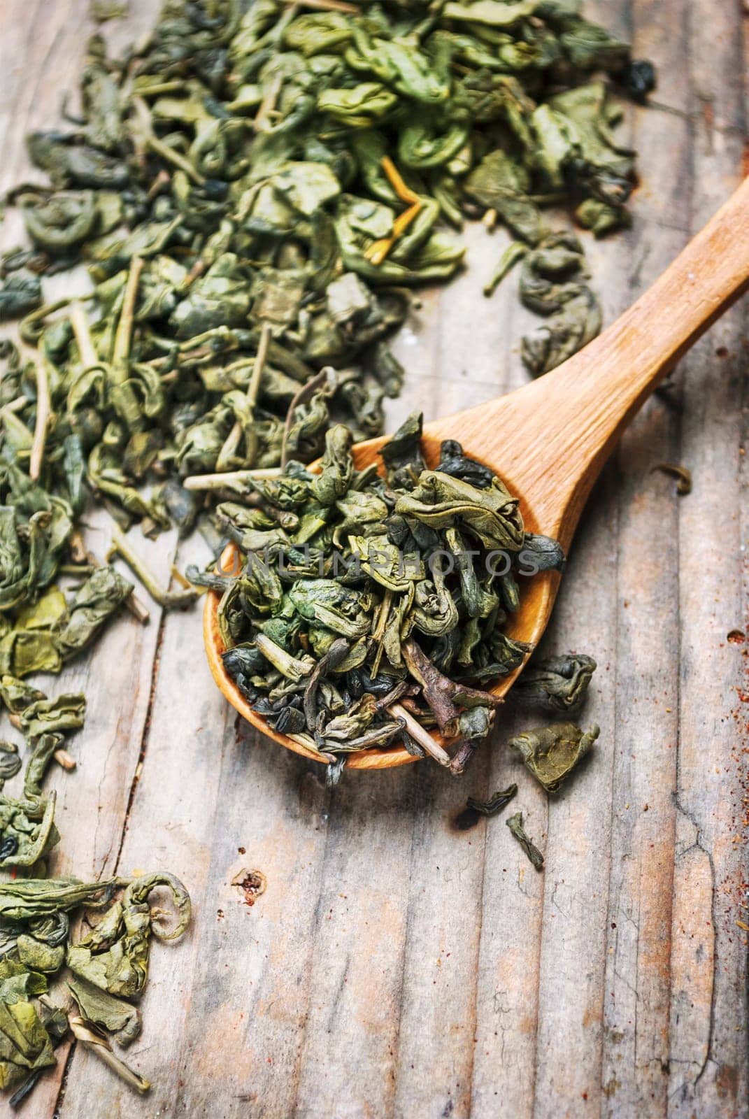 Dry green tea leaves in wooden spoon from above. Organic asian green herbal tea on vintage wooden table background.