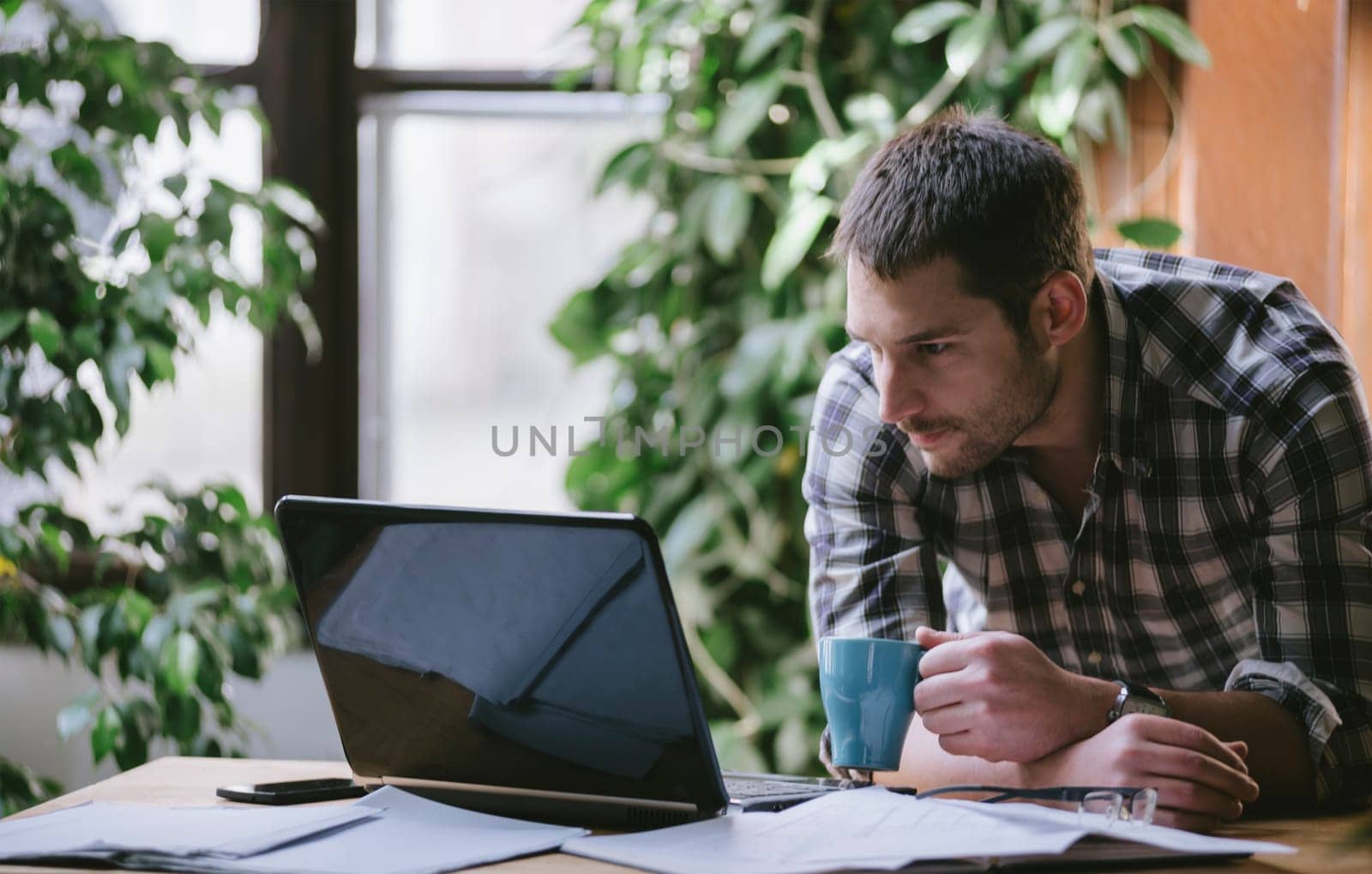 Young business man work on computer in his pleasant studio home office. Freelance professions in cool workplace environment: programmer, designer, architect, blogger, entrepreneur, social media. Natural light.