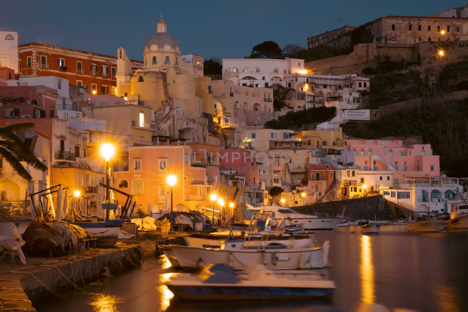 View of the Port of Corricella with lots of colorful houses at night in Procida Island, Italy.