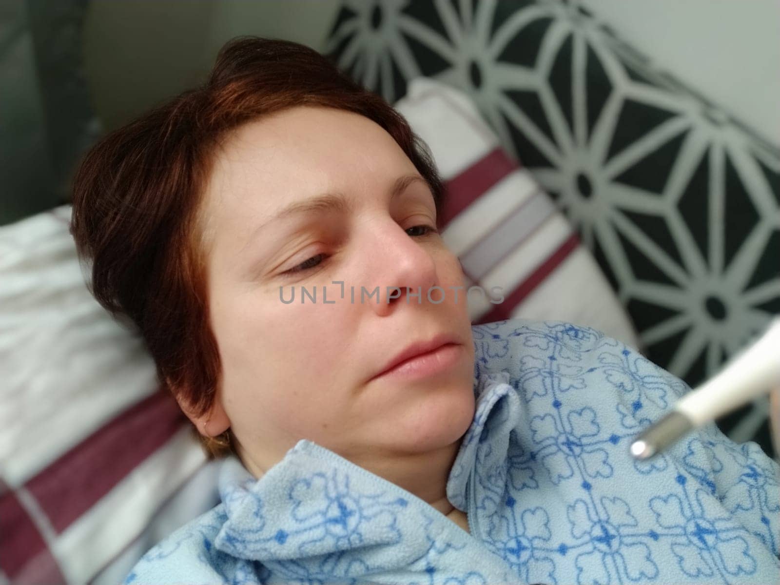 Sick woman in bed. Headache, runny nose and cold. Paleness of the face and faintness of the body. Feeling unwell. The patient lies on a pillow, holds a thermometer and measures the temperature
