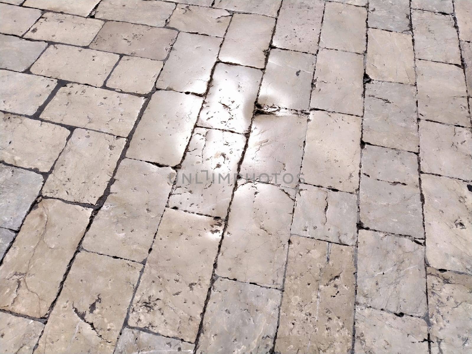 Marble floor on the street, Dubrovnik, Croatia. Antique masonry tiles rectangular blocks. Metamorphic rock composed of calcite CaCO3 mixed with other minerals. Polished tiles glisten in the sun.