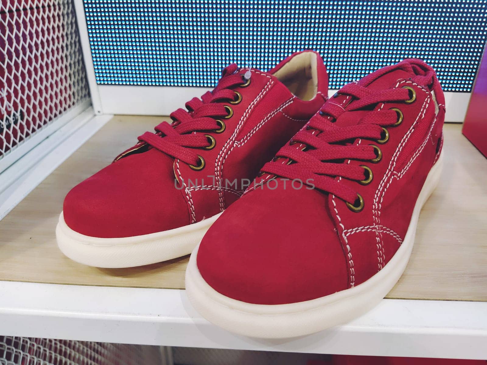 Red sneakers or sneakers made of natural suede on a store shelf. White flexible sole and red laces. Shoe shop. Youth comfortable fashionable shoes. Newest concept. The best red running shoes
