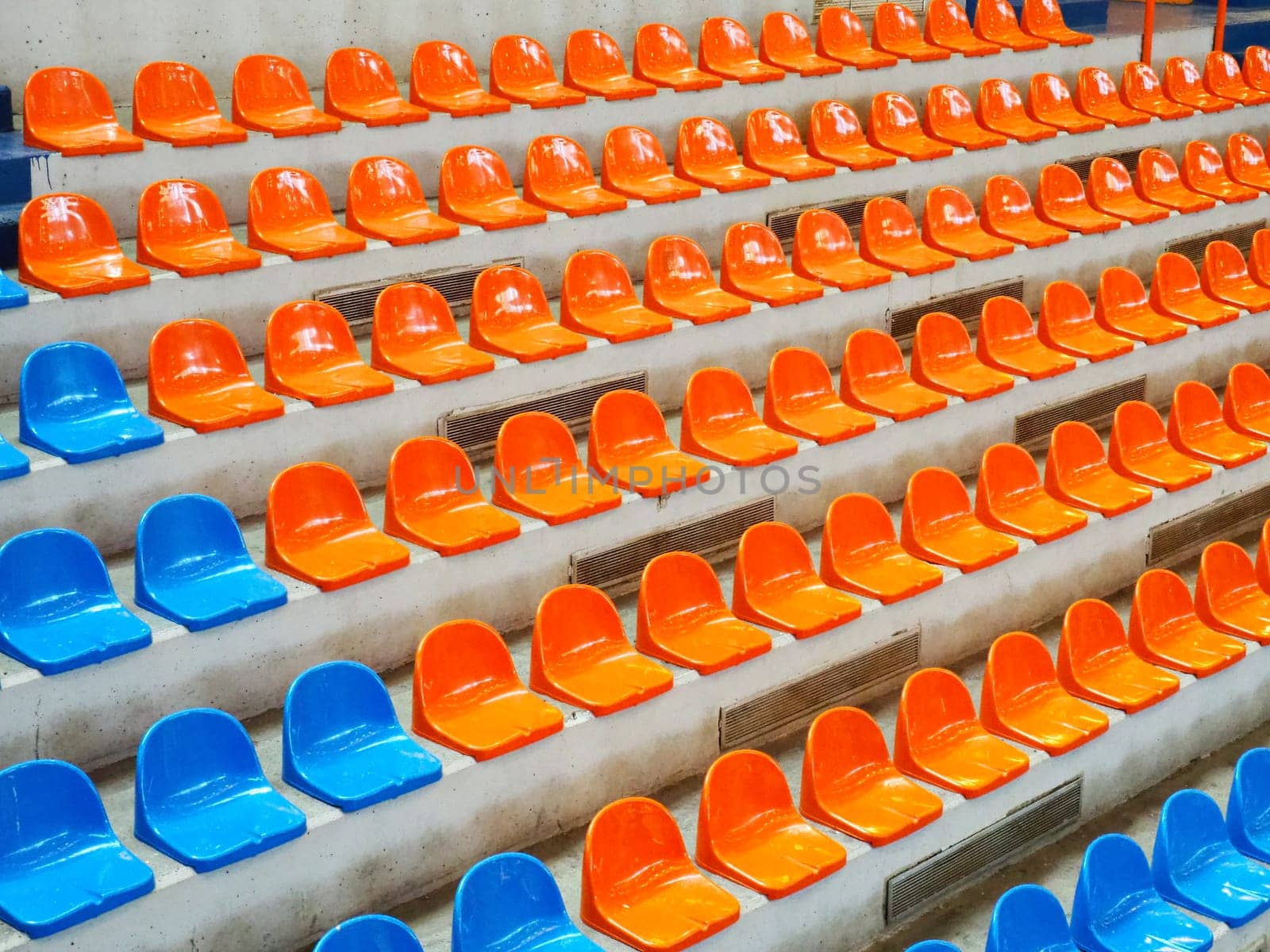 Bleachers, empty seats in the stands of the arena or auditorium. Rows of blue and orange stadium seats without spectators. The concept of the abolition of sports and mass entertainment events.