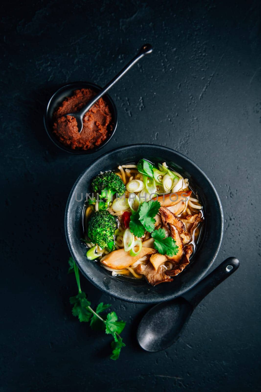 Vegan miso or ramen soup with mushrooms and vegetables on black background
