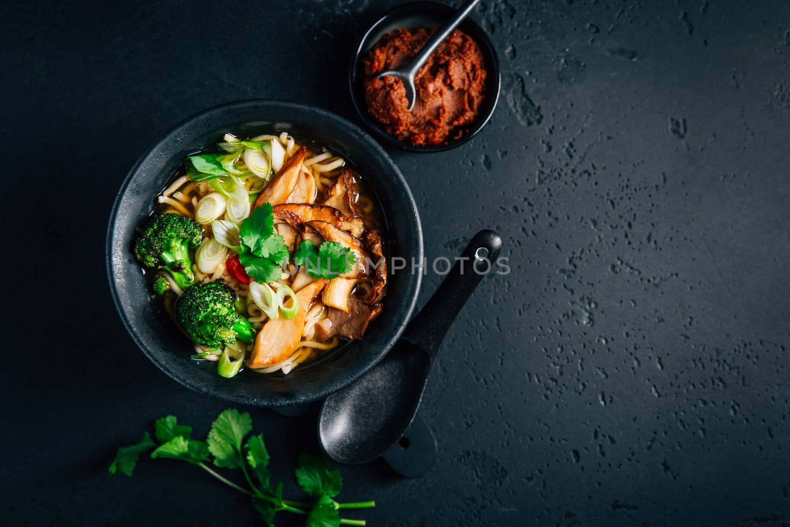 Vegan miso or ramen soup with mushrooms and vegetables on black background