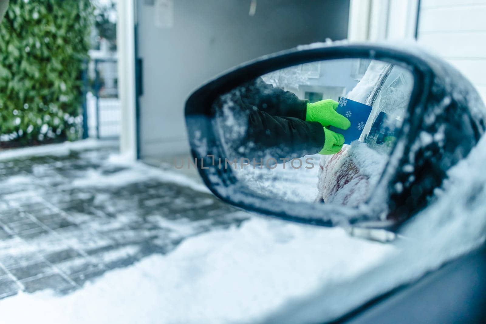 Teenager cleans car after a snowfall, removing snow and scraping ice