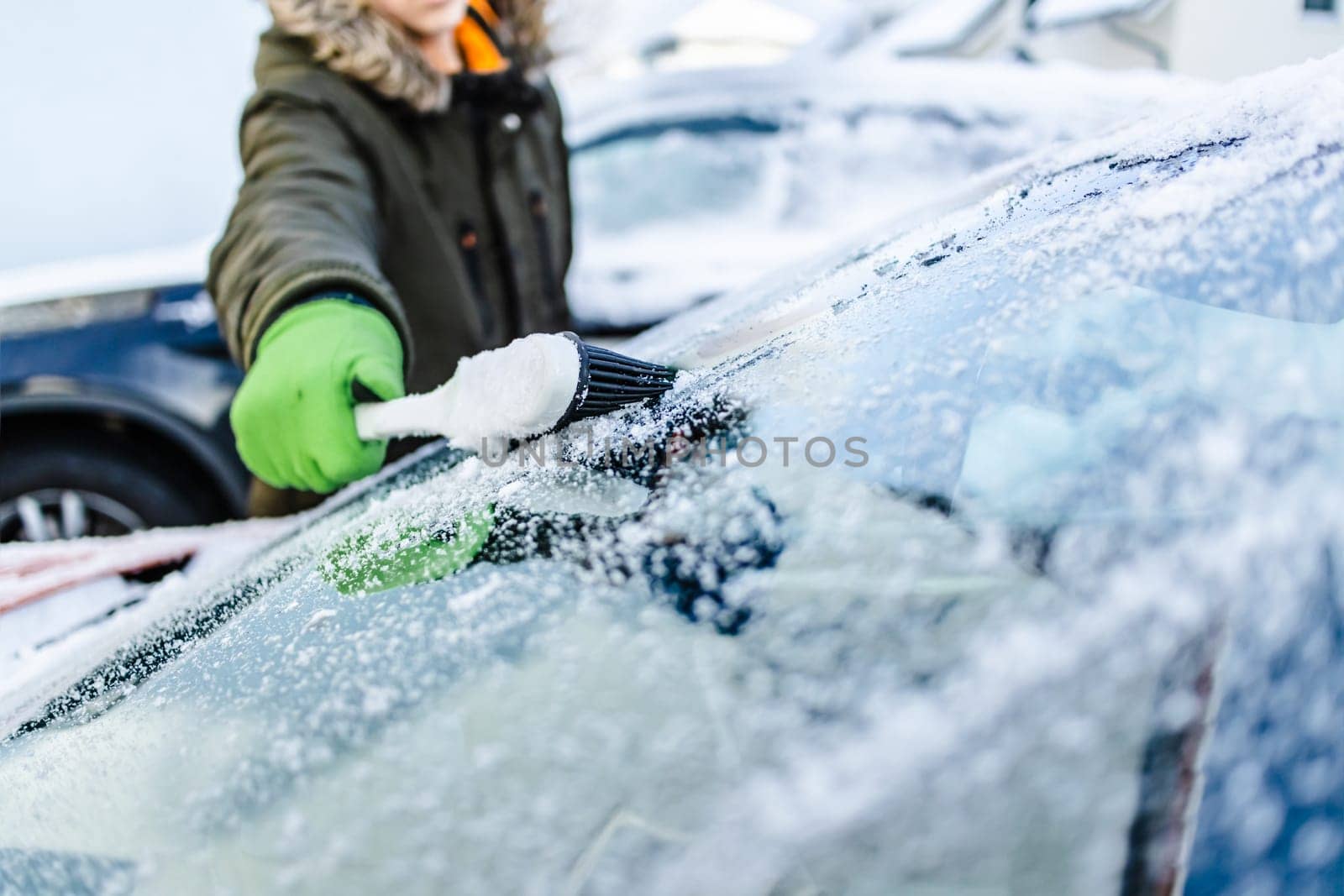 Teenager cleans car after a snowfall, removing snow and scraping ice