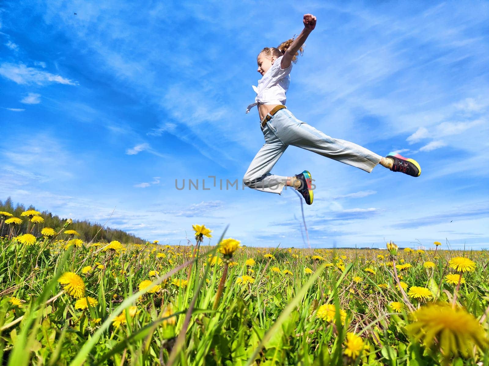A person expresses happiness by jumping in a lush field of dandelions, surrounded by a clear blue sky on a sunny day.