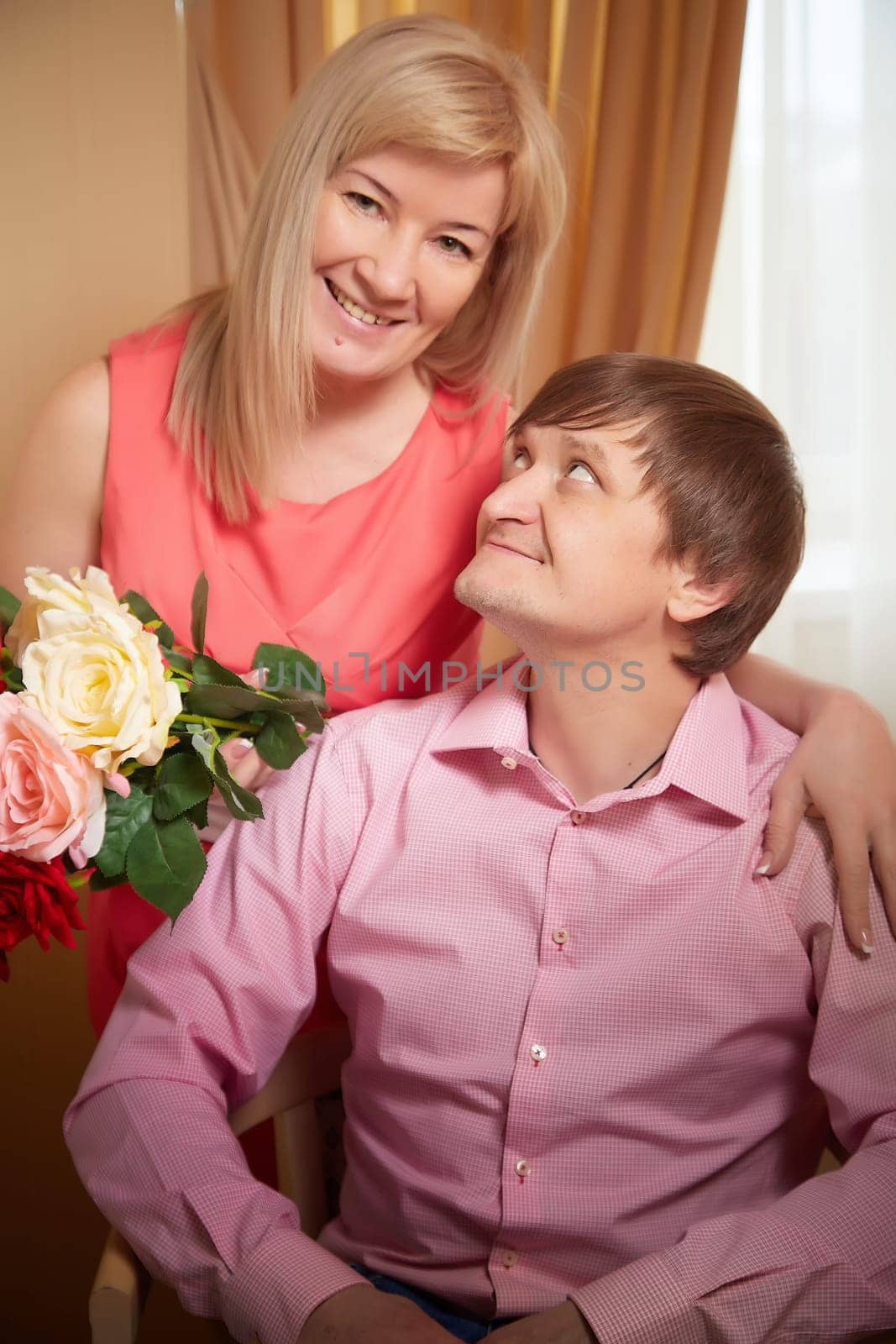 A middle-aged couple smiles affectionately during a photo shoot, showcasing their love and joy in a cozy hotel setting.