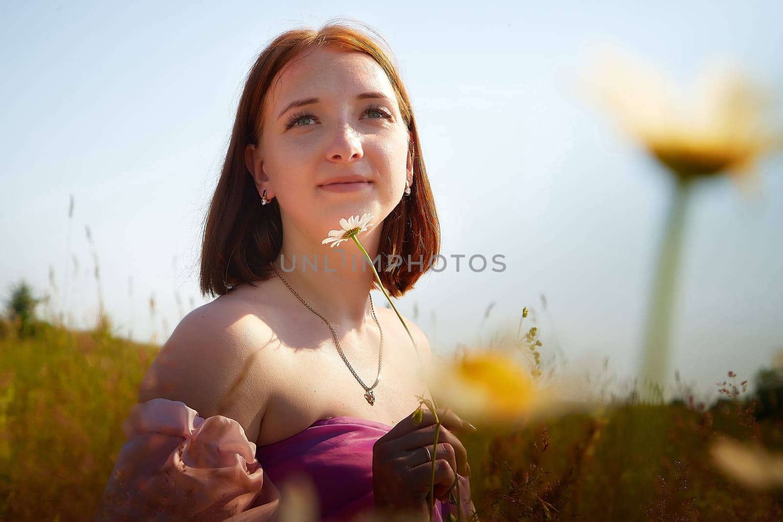 A young woman enjoys the beauty of nature, holding a flower while surrounded by a vibrant field on a sunny afternoon.