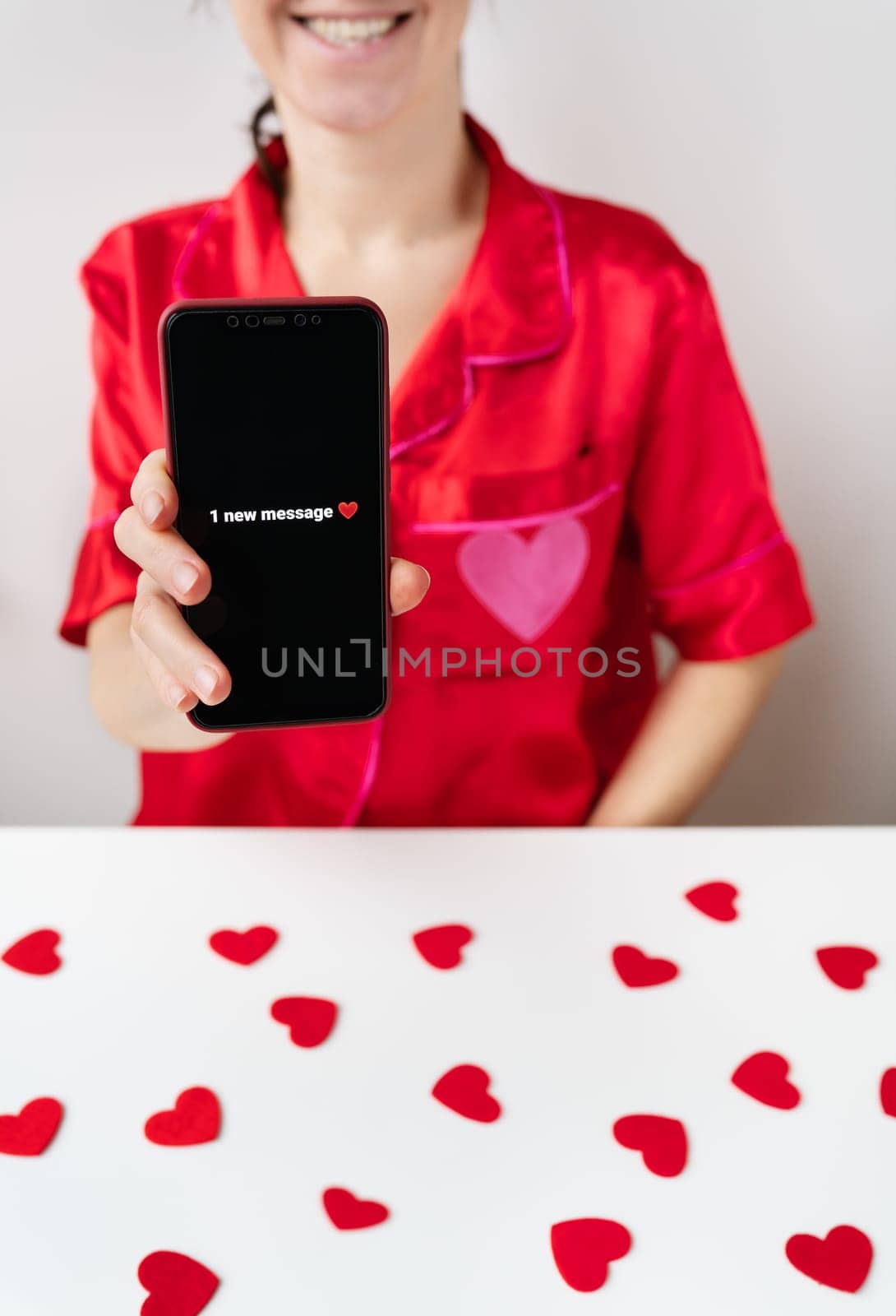 A happy girl is holding a smartphone with an activated screen with 1 SMS message in the shape of a heart. Concept of Valentine's Day, February 14