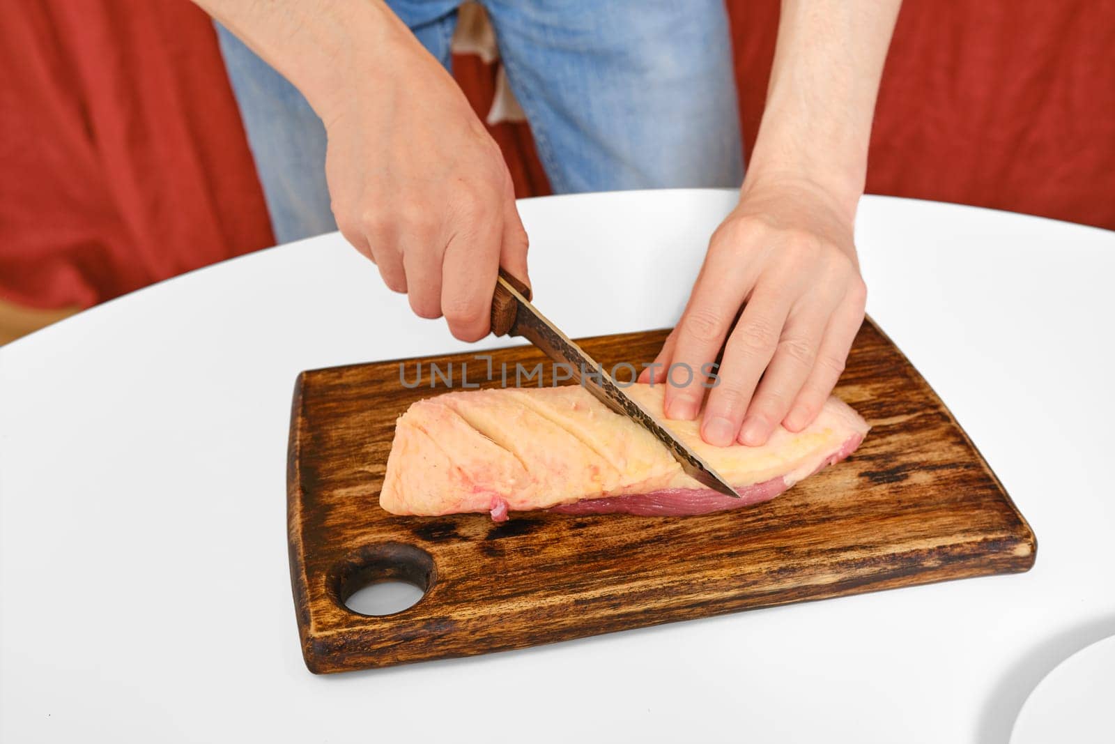 unrecognizable man cuts the skin crosswise on a duck breast