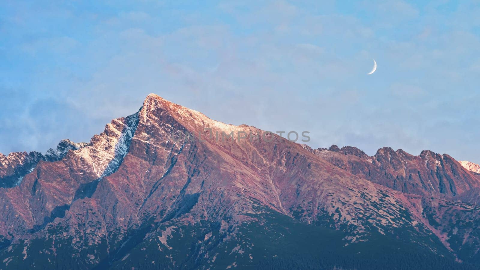 Crescent moon rising over mount Krivan peak - Slovak symbol - forest trees silhouettes in foreground, evening scene.