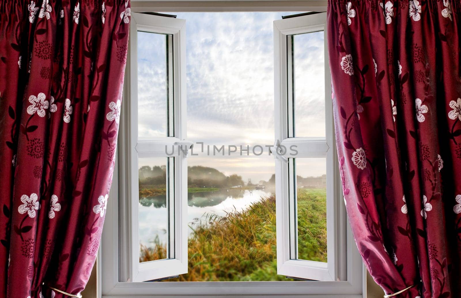 Beautiful rural view out of an open window with red curtains. Looking on to a canal waterway at sunrise in Norfolk England