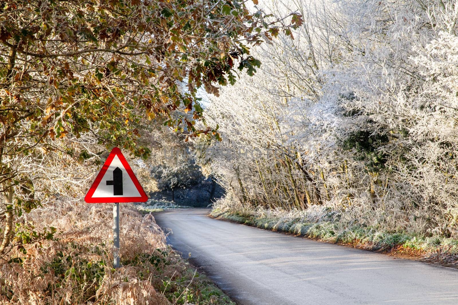 Frozen winter rural road with triangle warning sign and lined with beautiful frosty trees.