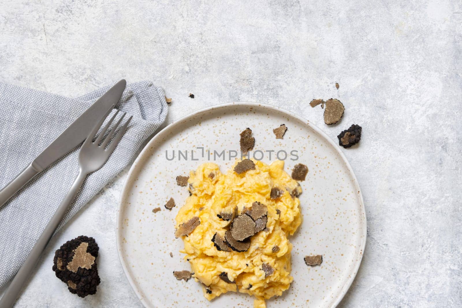 Scrambled eggs with sliced fresh black truffles from Italy served in a plate near fork and knife top view. Italian cousine, gourmet breakfast