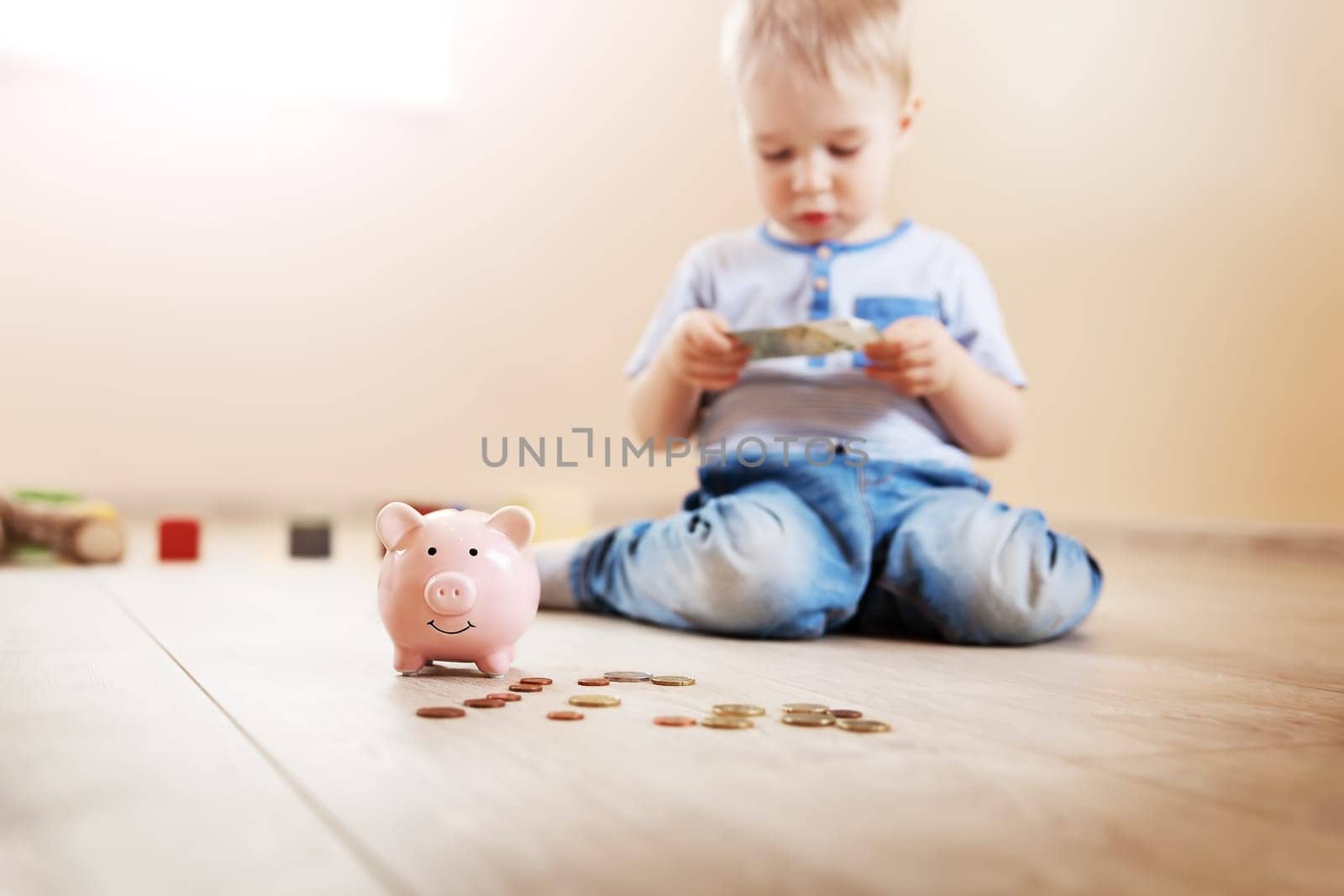 Cute boy sitting on the floor indoor and inserting euro coins in piggybank. Concept of the economy and family budget.