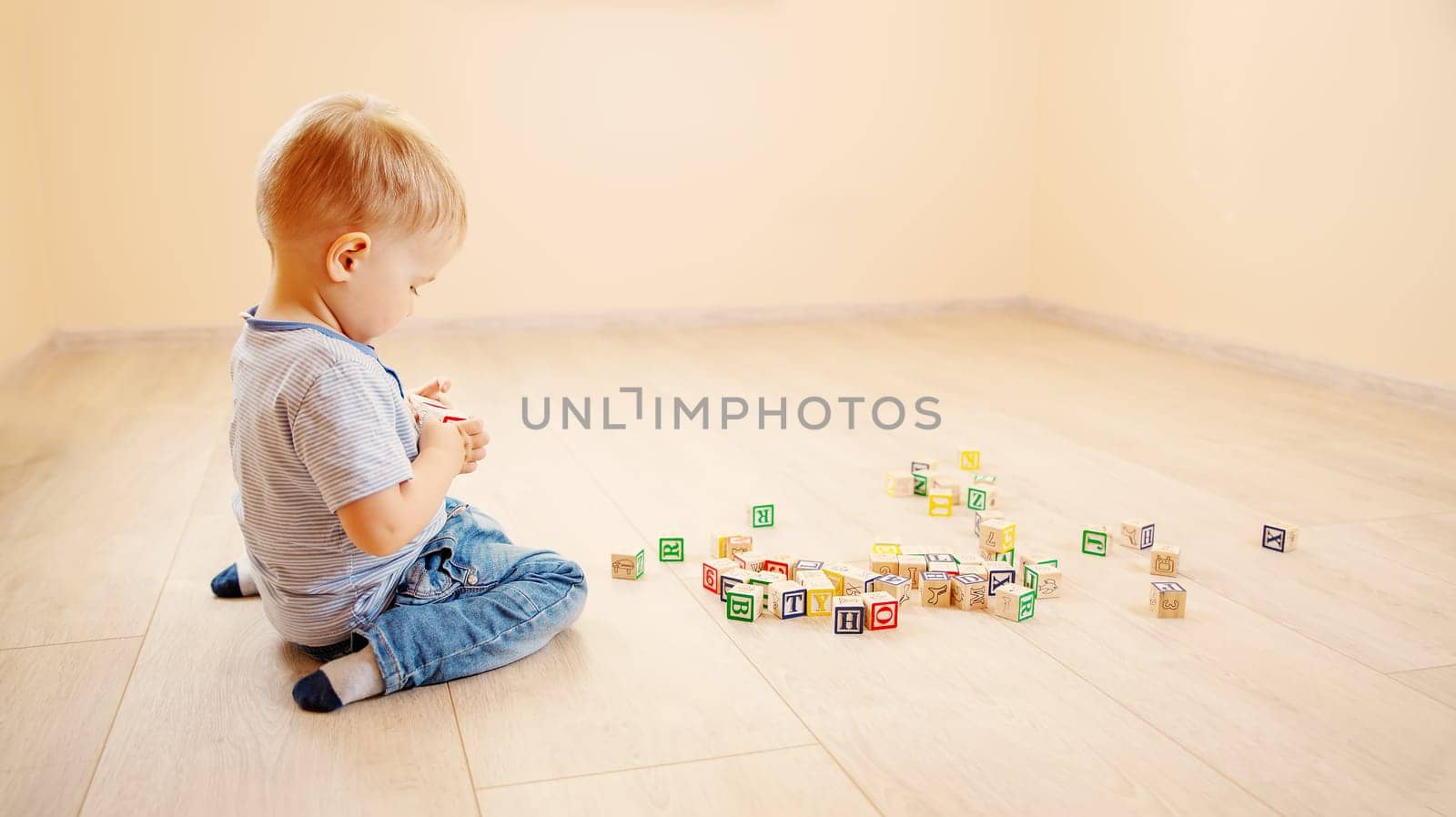 Little boy sitting on the floor indoor and playing with wooden cubes. Concept of preschool and kindergarden.