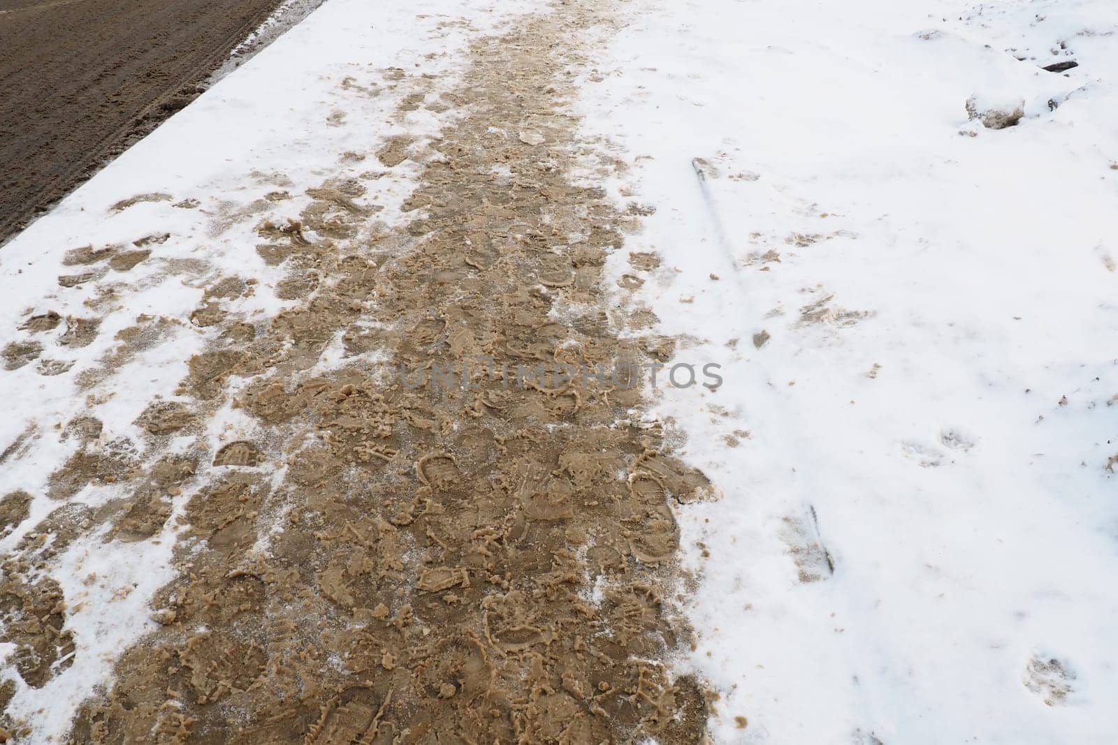 Many footprints of shoes and boots on the snowy pavement. Winter in the city. Wet weather and freezing temperatures. Weather forecast. Ice, white snow and muddy tracks with clay on the road