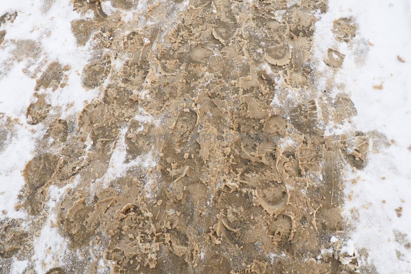 Many footprints of shoes and boots on the snowy pavement. Winter in the city. Wet weather and freezing temperatures. Weather forecast. Ice, white snow and muddy tracks with clay on the road