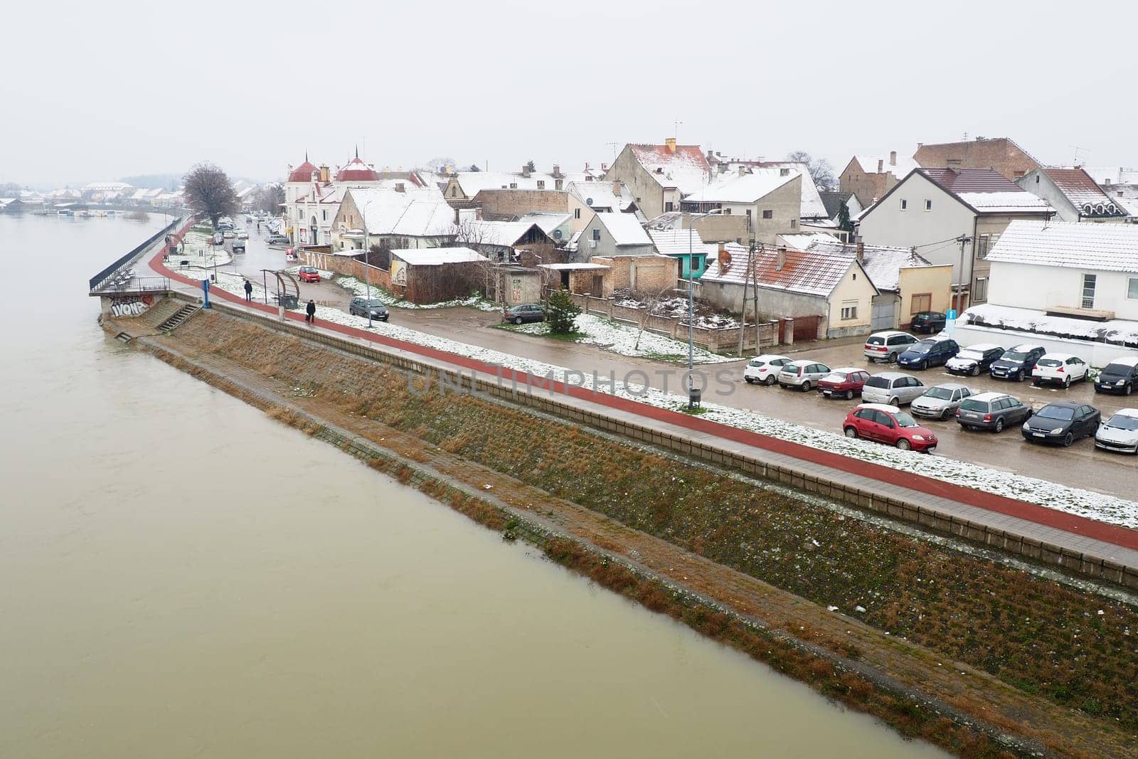 Sremska Mitrovica, Serbia 01.27.2023 View from the bridge over the Sava River. Flooding after heavy rains and snowmelt. Muddy water. Winter cityscape. People go and ride bicycles, cars go. Embankment