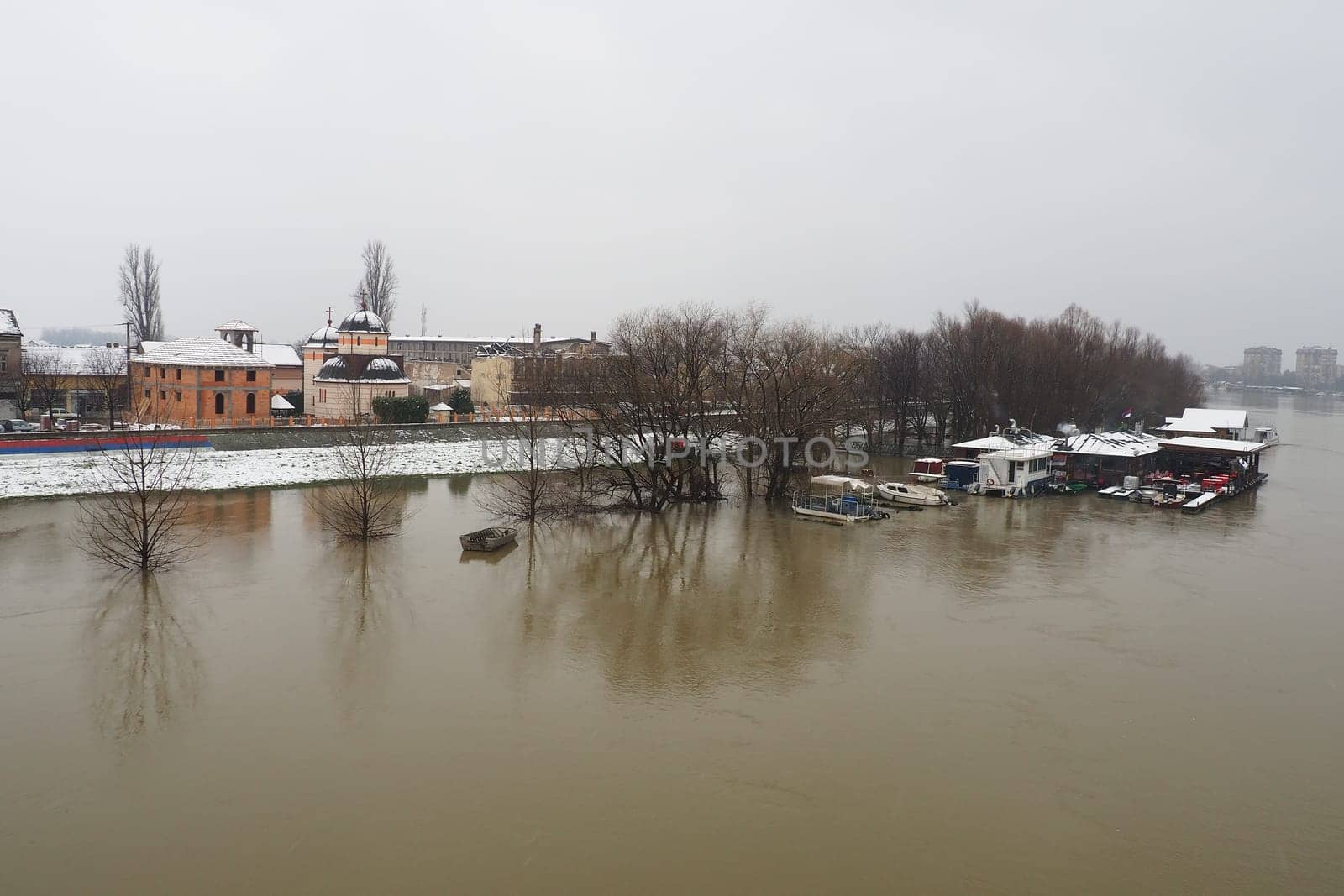 Macvanska Mitrovica, Serbia, 01.27.2023 The bridge over the Sava River. Flooding after heavy rains and snowmelt. A swift flow of muddy water. Trees, boats and piers in the water. Machva in winter