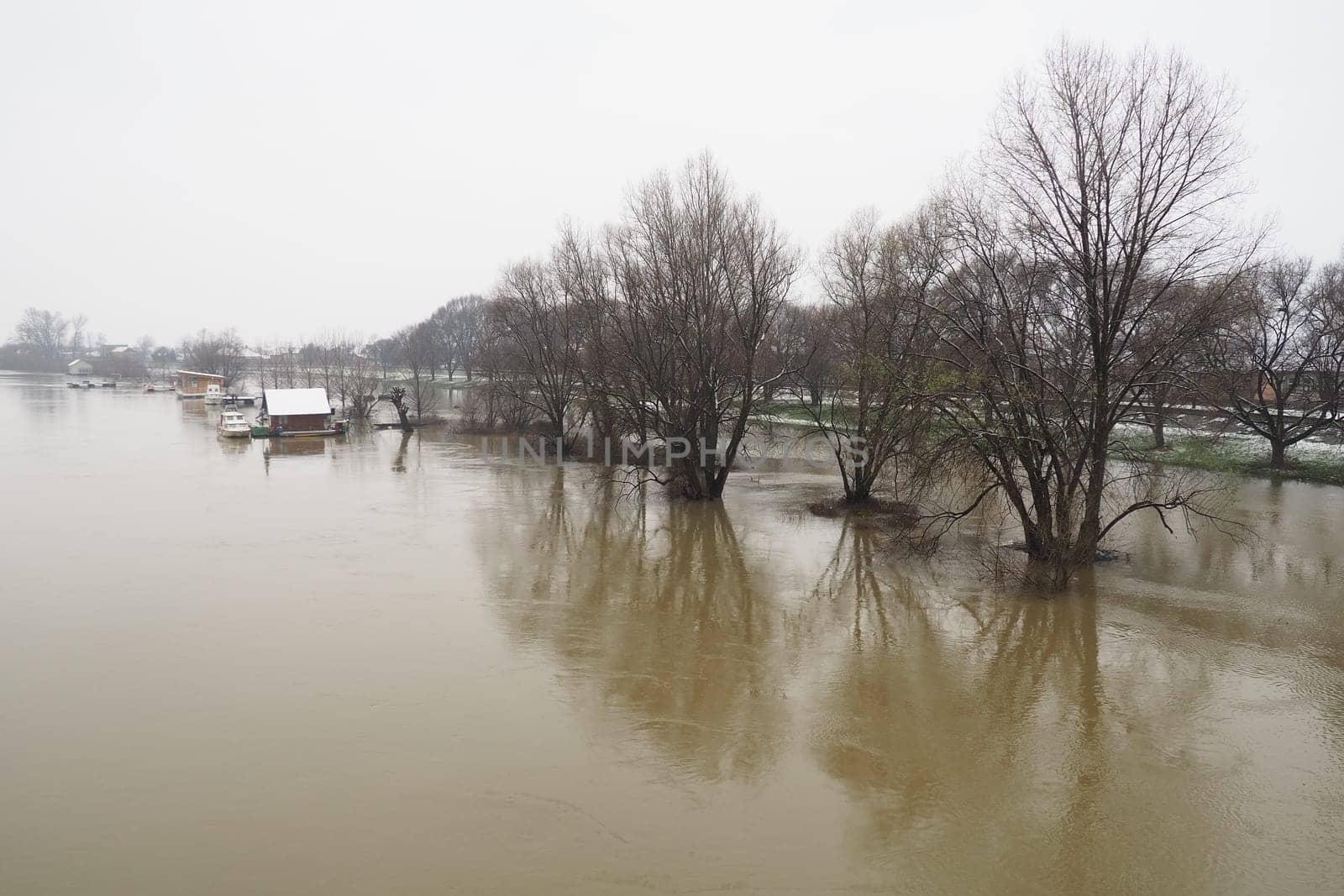 Macvanska Mitrovica, Serbia, 01/27/2023 The bridge over the Sava River. Flooding after heavy rains and snowmelt. A swift flow of muddy water. Trees, boats and piers in the water. Machva in winter